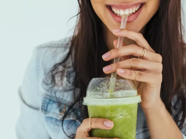Woman drinking green smoothie while smiling