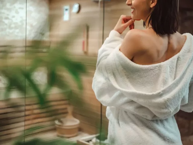 Woman in robe entering steam room with bucket