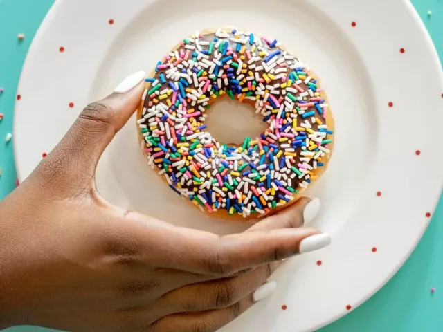Woman holding a sprinkled chocolate donut, which has unhealthy trans fats