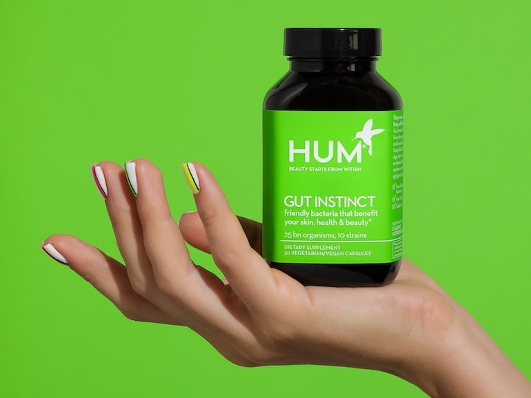 Woman's hand holding HUM Gut Instinct probiotic supplement in front of green background