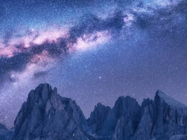 Purple and blue starry night sky above mountains