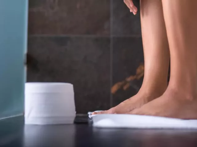 Woman sitting on toilet next to a roll of toilet paper