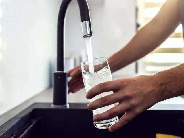 Close up of man getting a glass of water from the kitchen sink since he knows it's important to stay hydrated
