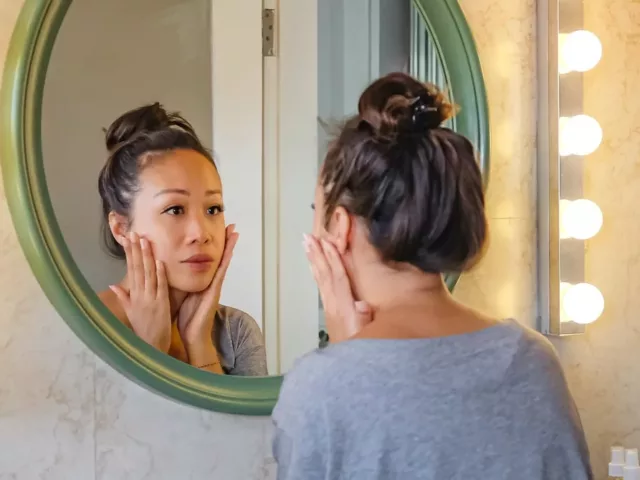 Worried woman looking at her face in the mirror and investigating skin purging from a new product