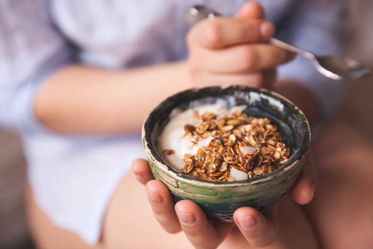 Woman holding a Greek yogurt bowl topped with seeds for a healthy, high-protein lunch