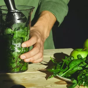 Man mixing a smoothie with various types of leafy greens to reap their health benefits