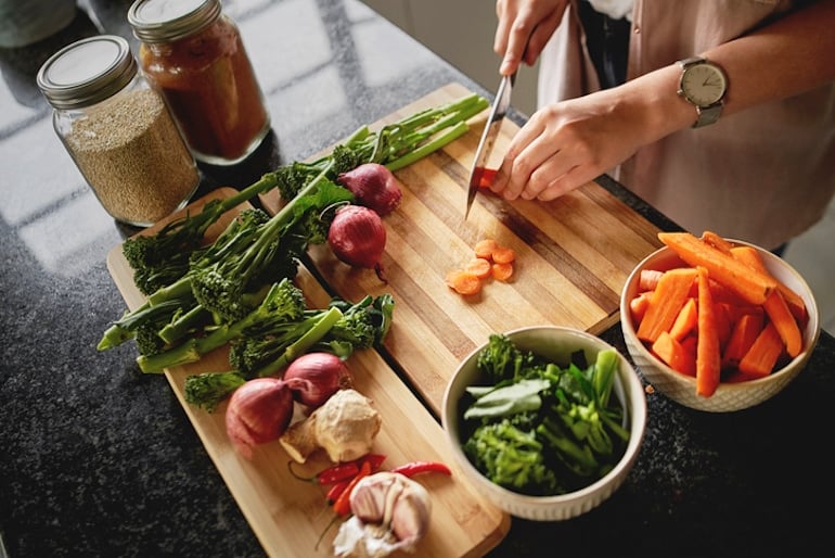 Overhead angled shot on woman chopping vegetables on a cutting board; healthy diet concept