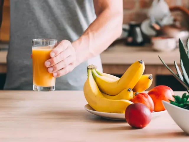 Man in kitchen holding juice with bananas and apples to help reduce bloating