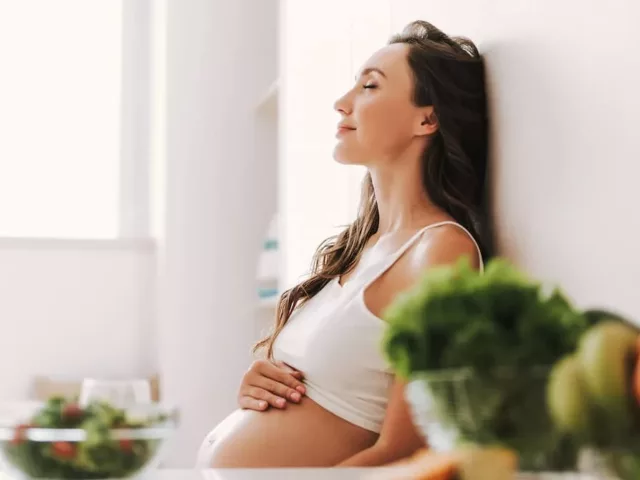 Pregnant woman with long hair sitting in the kitchen after taking a prenatal vitamin